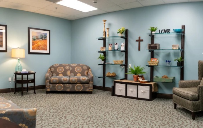 A cozy waiting room with a patterned couch, decorative shelves, and a cross on the wall.
