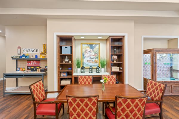 A well-decorated dining area featuring a wooden table with red upholstered chairs, surrounded by bookshelves and artwork on the wall.
