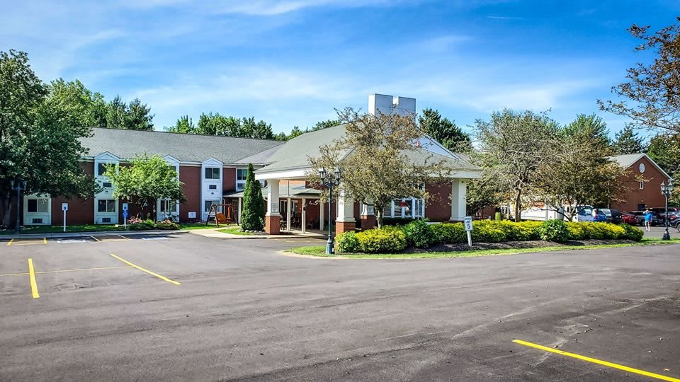 A hotel building with a landscaped entrance and spacious parking area under a clear blue sky.