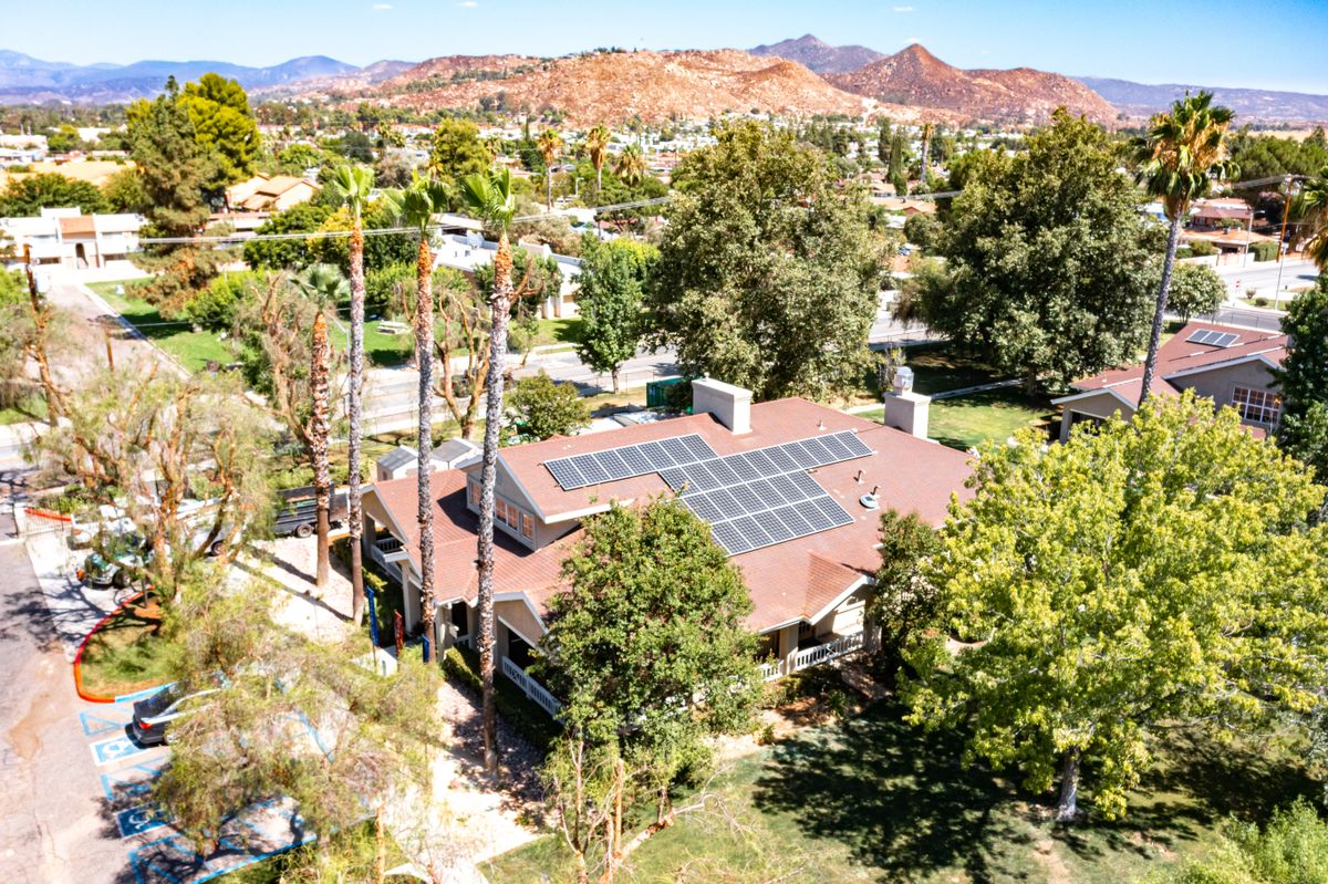 A suburban house with solar panels surrounded by trees, captured from an aerial view.