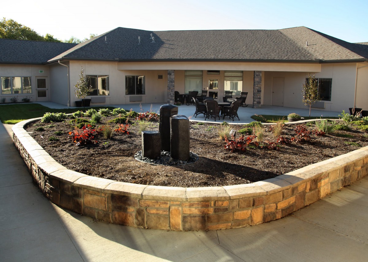 A beautifully landscaped garden with a fountain and outdoor seating area in front of a house.