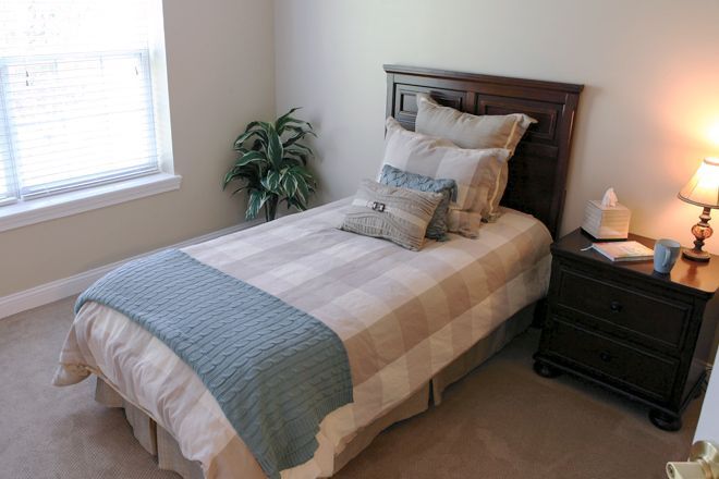 A neatly made single bed with multiple pillows and a bedside table in a well-lit bedroom.