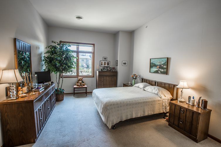 A cozy bedroom featuring a neatly made bed, wooden furniture, and a large window with natural light.
