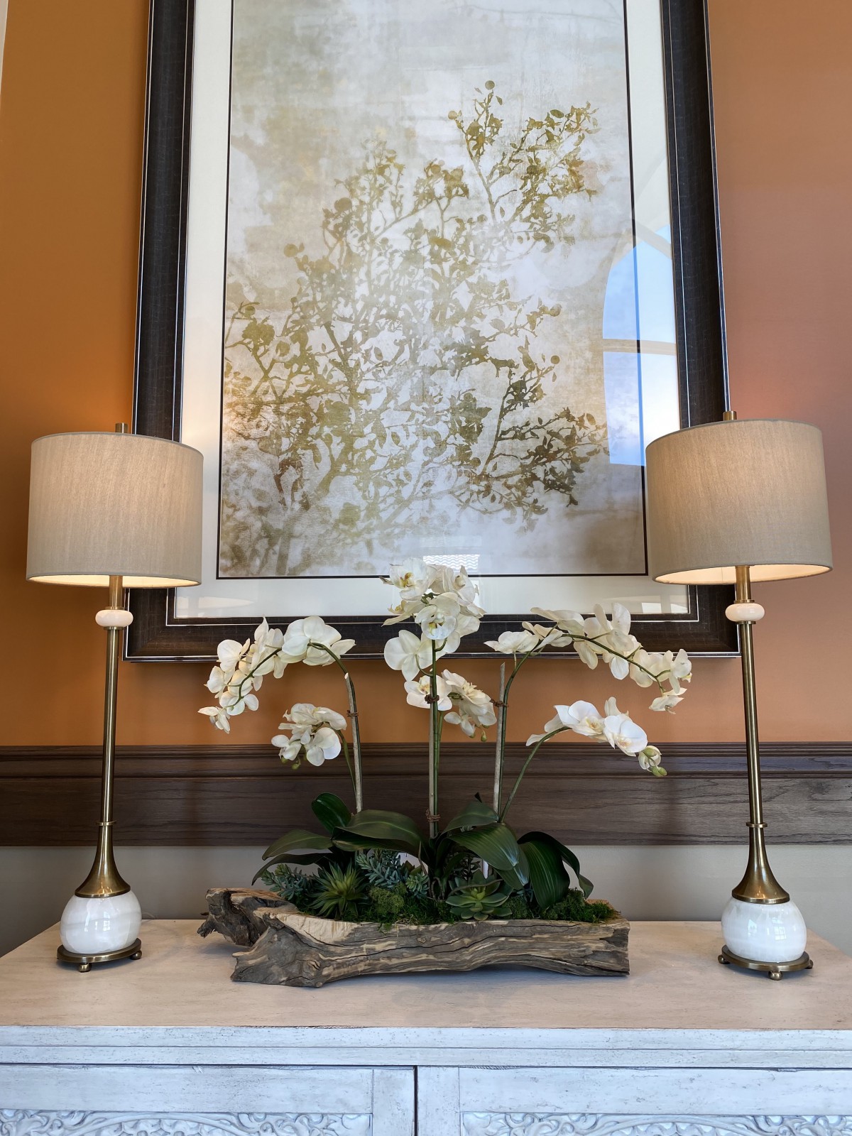 A stylish home interior setup featuring two elegant lamps flanking a floral arrangement, with a large abstract painting in the background.
