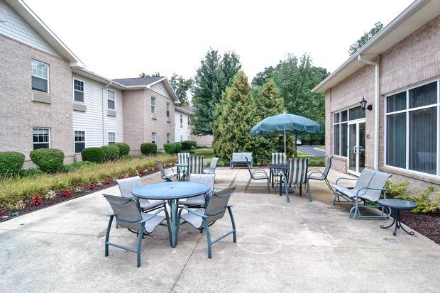 A residential patio area with outdoor seating, tables, and an umbrella surrounded by greenery.