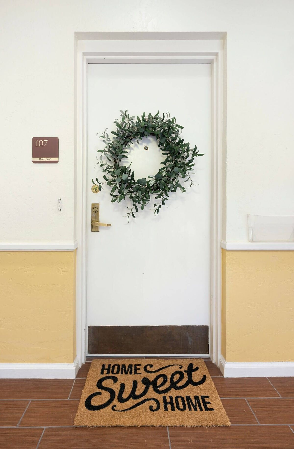 A decorated apartment door with a green wreath and a welcome mat.