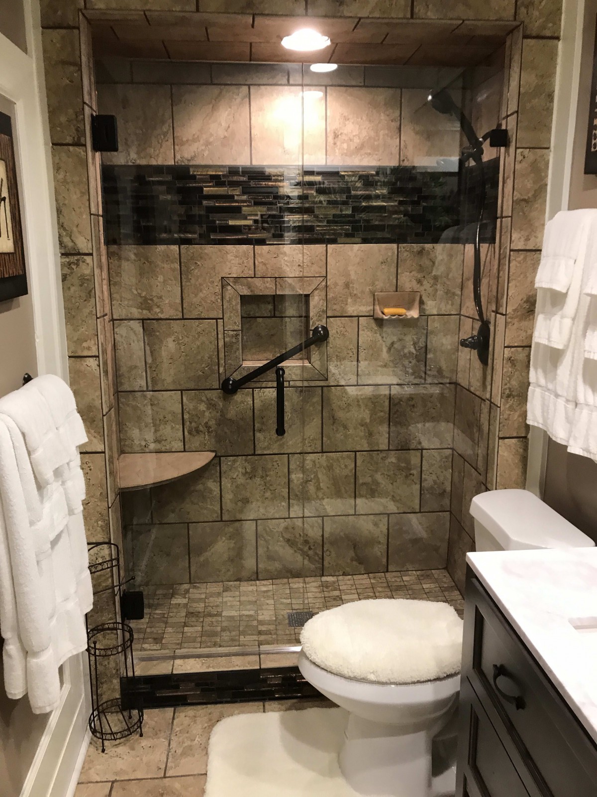A modern bathroom featuring a tiled shower with glass doors, a grab bar, and neatly arranged towels.