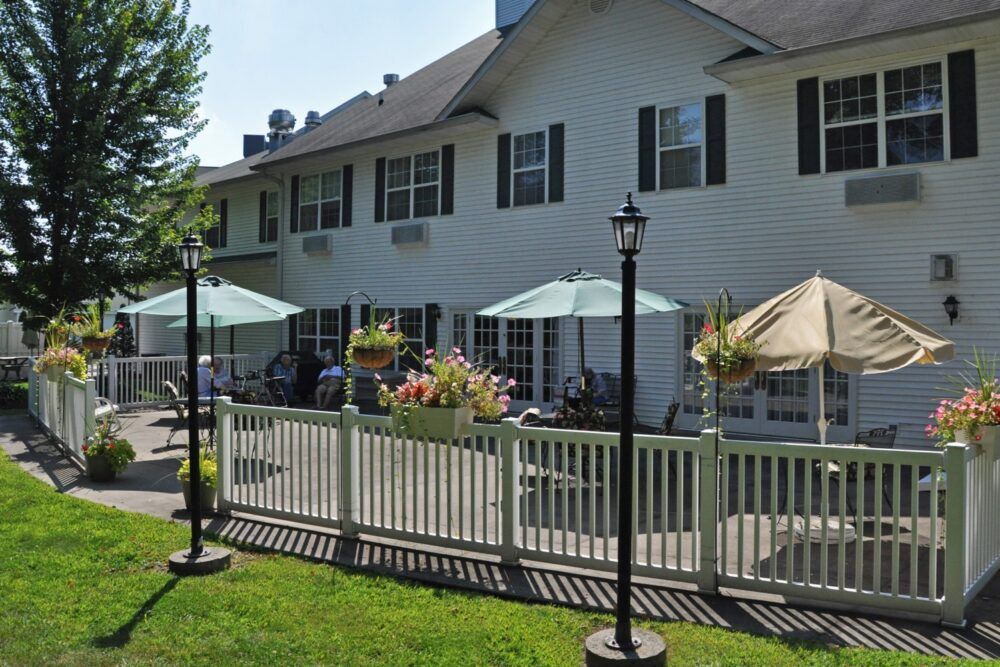 A residential building with a patio area featuring umbrellas and outdoor seating, surrounded by a white fence.