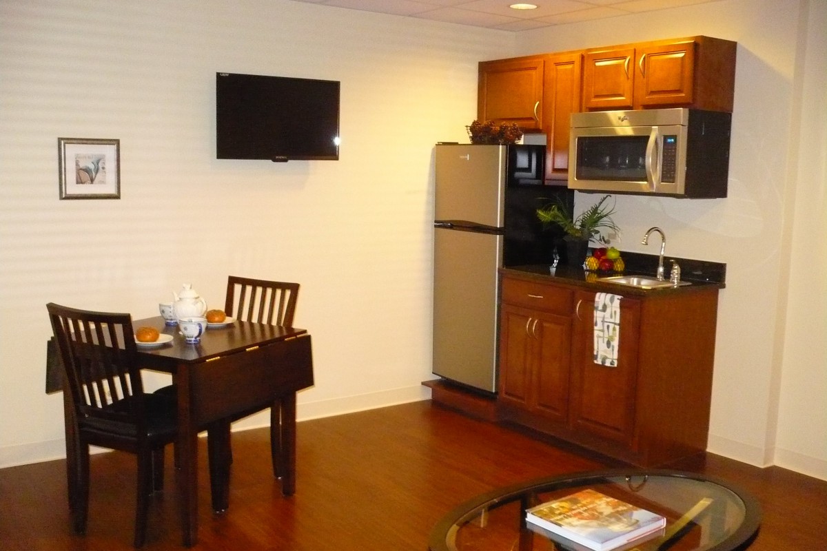 A small kitchen and dining area with wooden cabinets, a table, and a wall-mounted television.