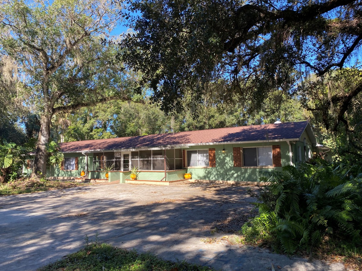 A single-story house surrounded by trees in a sunny setting.
