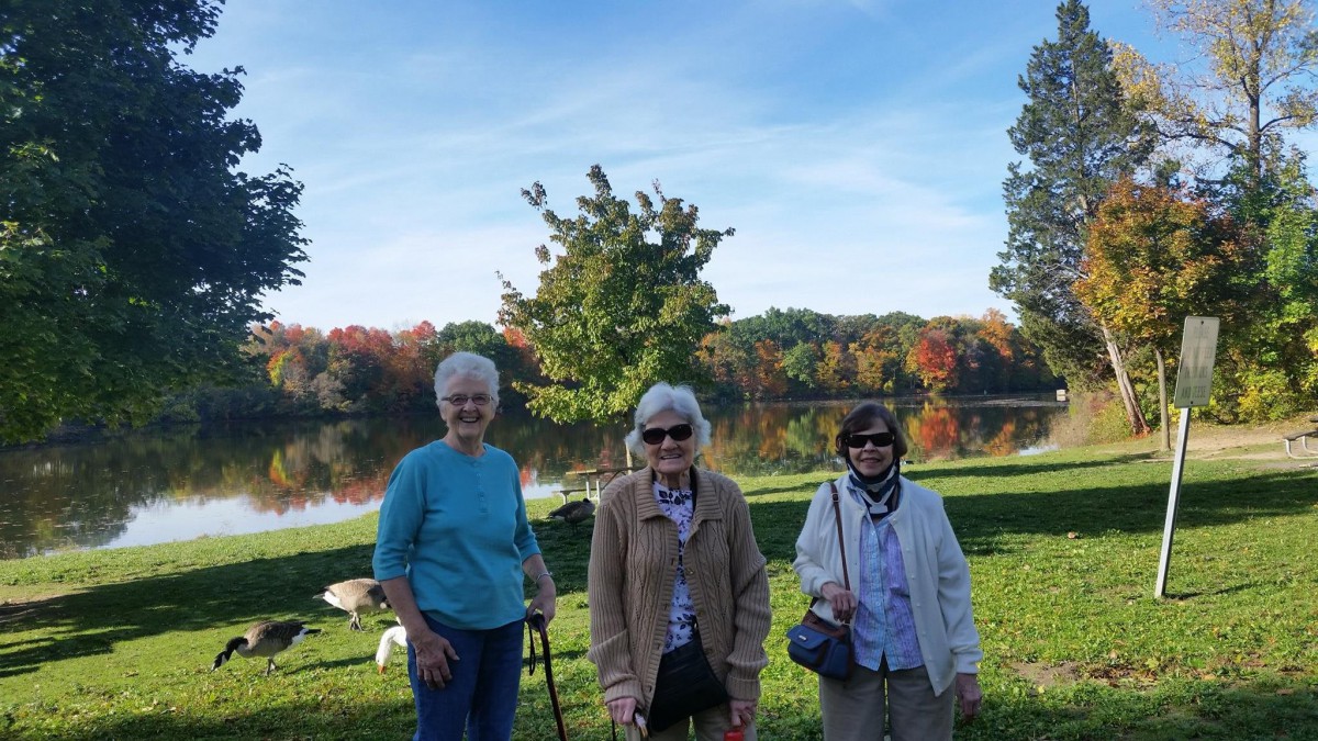 Three seniors enjoying a sunny day by the lake with autumn foliage in the background.