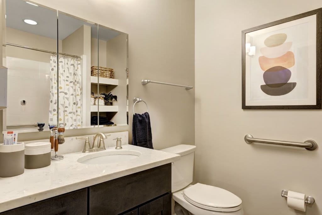 A modern bathroom with a sleek design, featuring a large mirror, sink, and toilet.