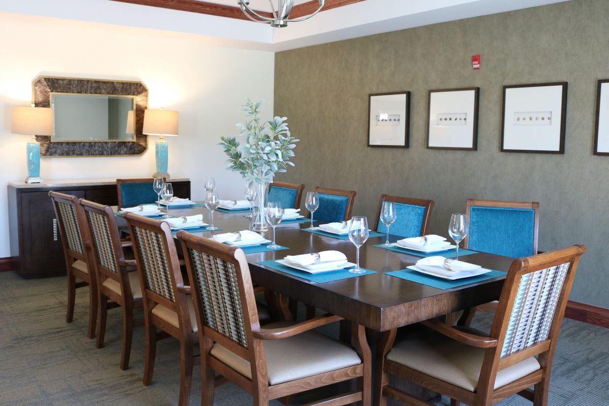 An elegant dining room setup featuring a long wooden table surrounded by chairs, with place settings and decoration.
