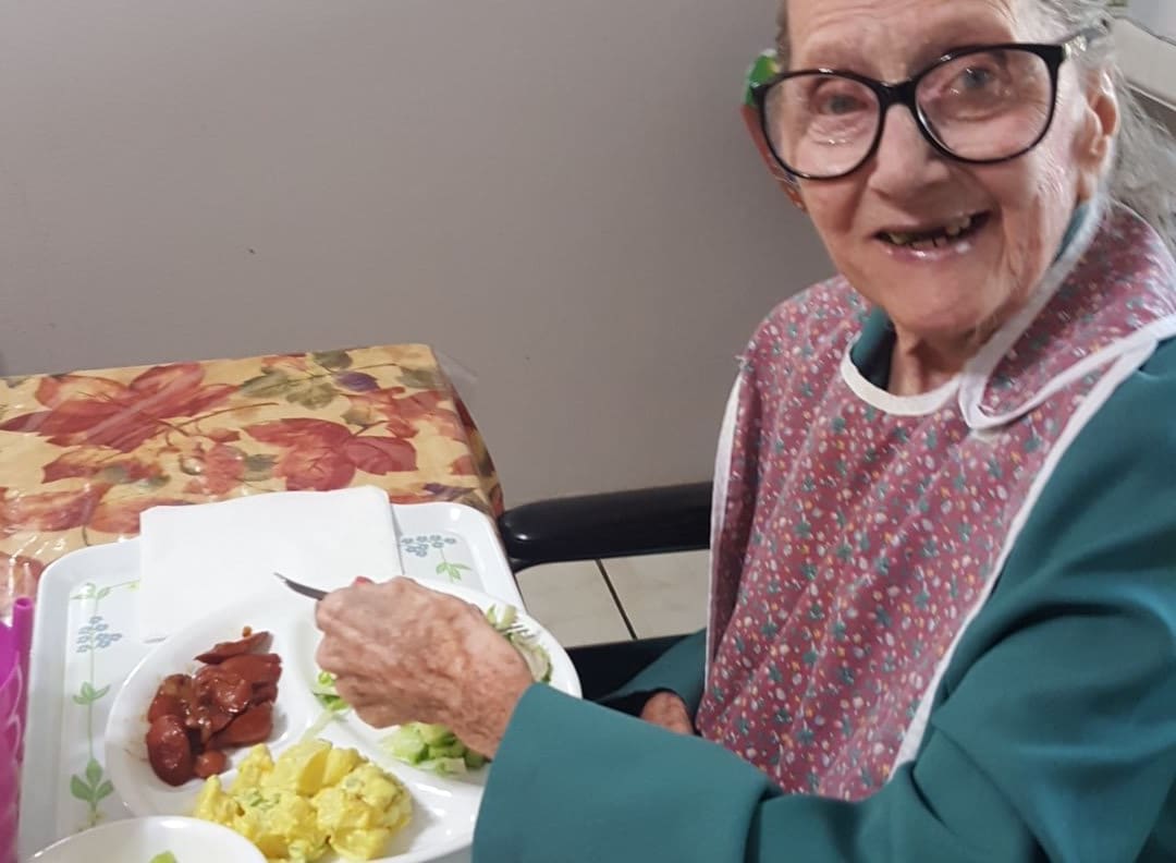 An elderly woman wearing glasses enjoys a meal indoors.