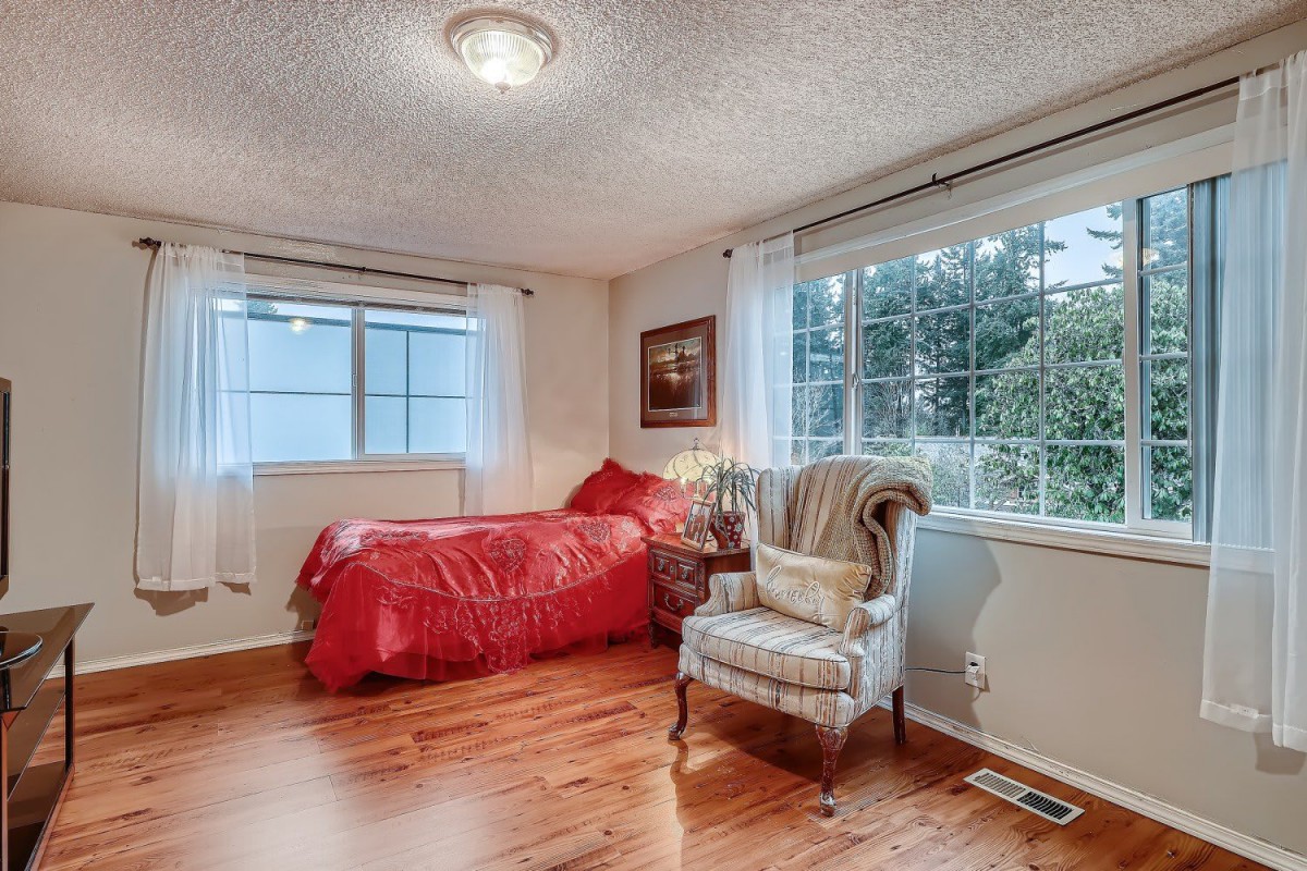 A cozy bedroom with red bedding, an armchair, and large windows allowing natural light to fill the space.