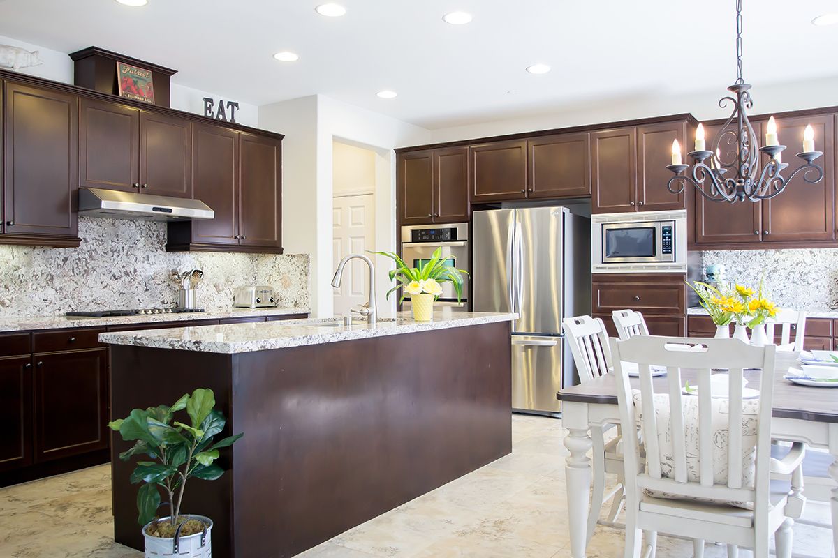 A modern kitchen featuring stainless steel appliances, wood cabinets, and a spacious dining area with a marble countertop.