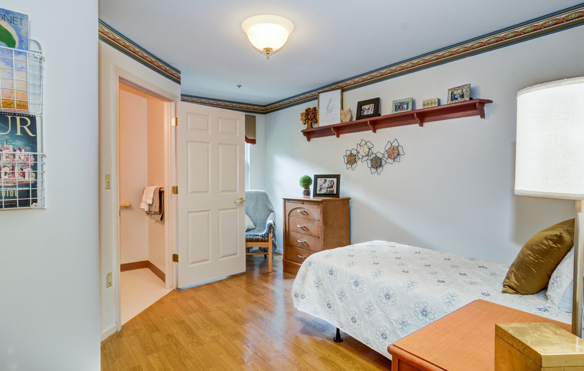 A cozy bedroom featuring a wooden floor, a bed with floral bedding, and decorative items on a wall shelf.