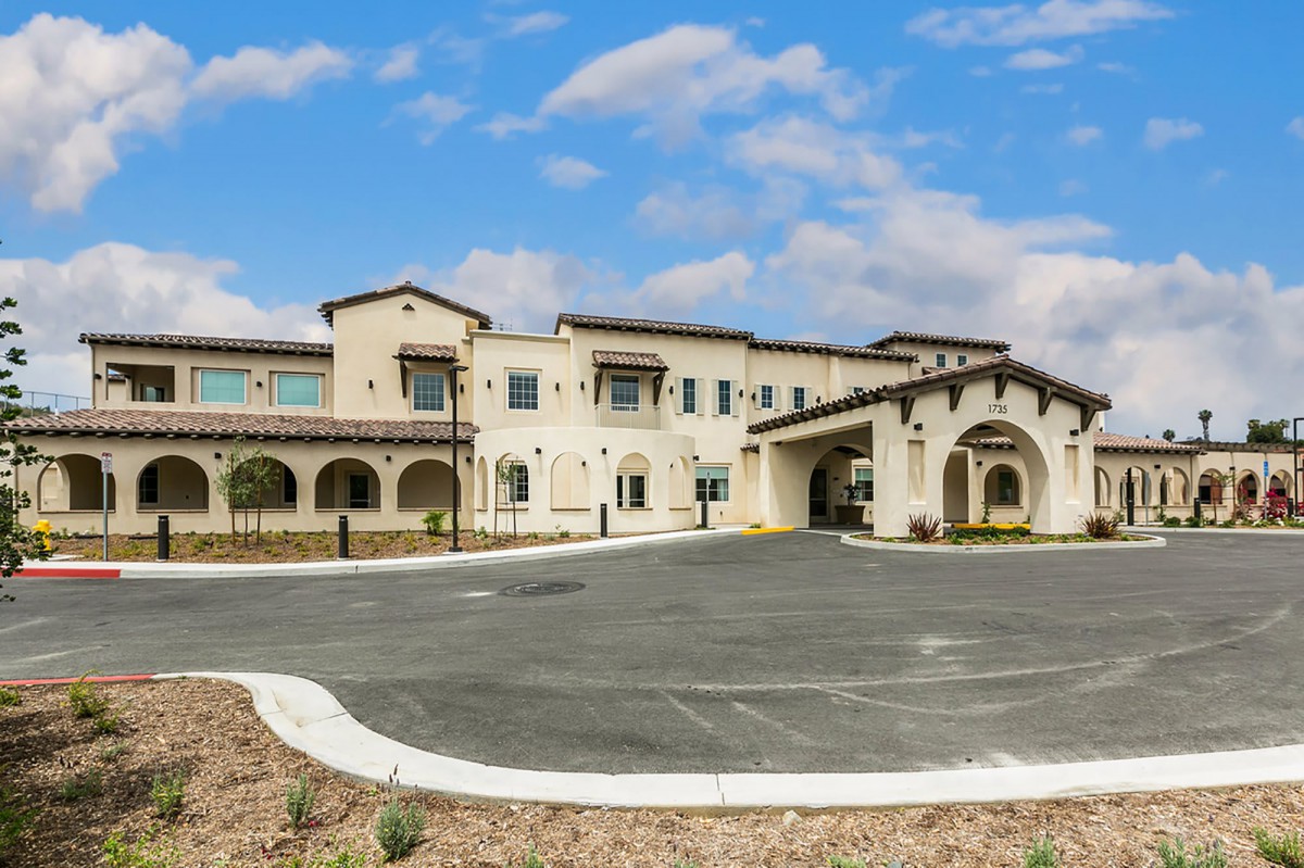 A modern residential building with a spacious driveway and a cloudy sky backdrop.