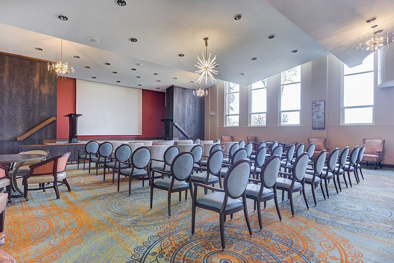 A well-lit conference room with rows of chairs facing a projector screen.