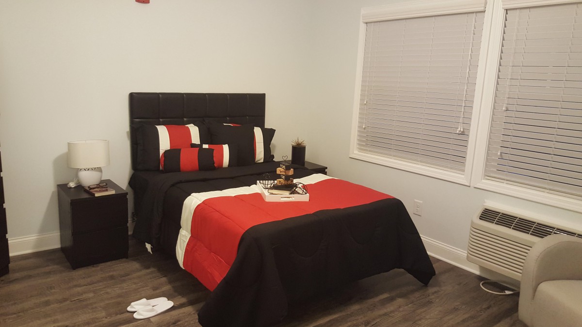 A neatly arranged bedroom featuring a black and red color scheme with a bed, pillows, and window blinds.