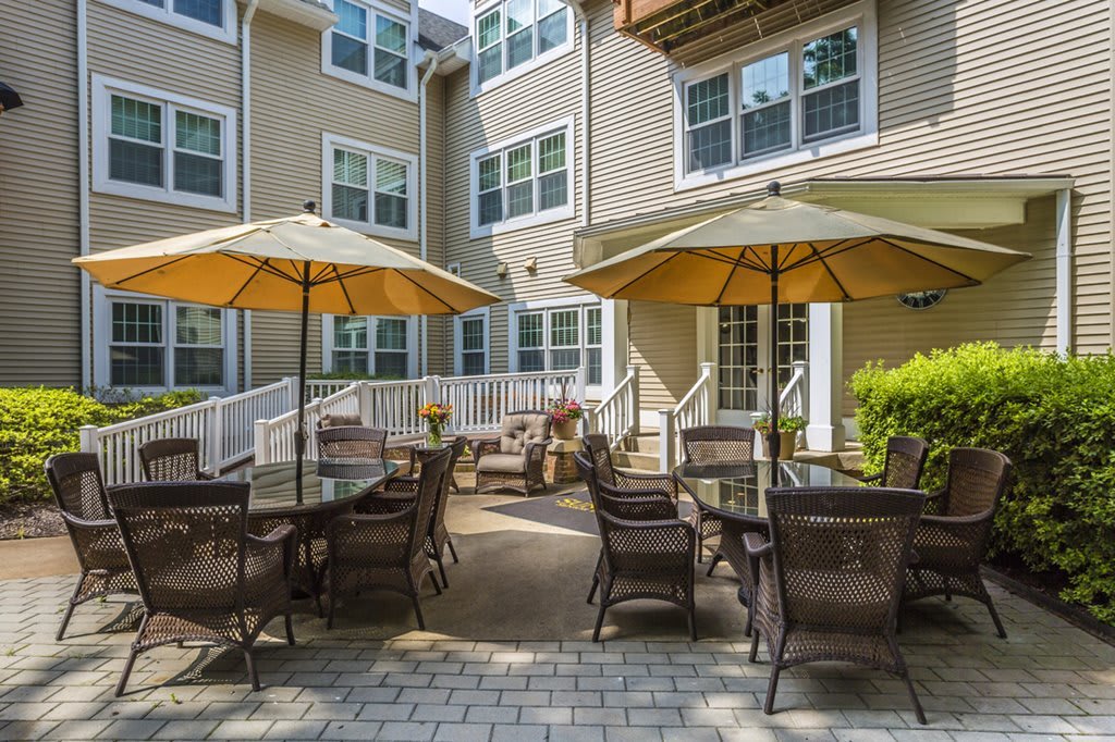 A cozy outdoor patio area with tables and chairs shaded by large umbrellas in a courtyard setting.