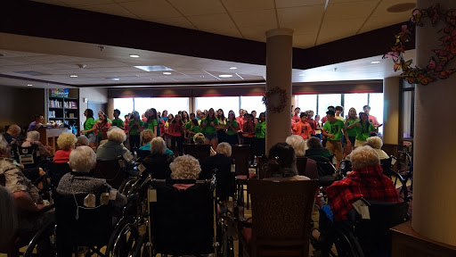 A joyful group performance taking place in a communal setting, with an engaged audience of seniors.