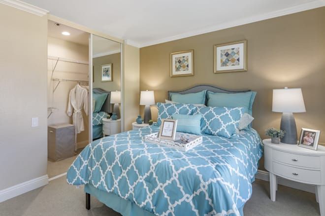 A cozy bedroom with blue and white bedding, mirrored closet doors, and elegant lamps on bedside tables.