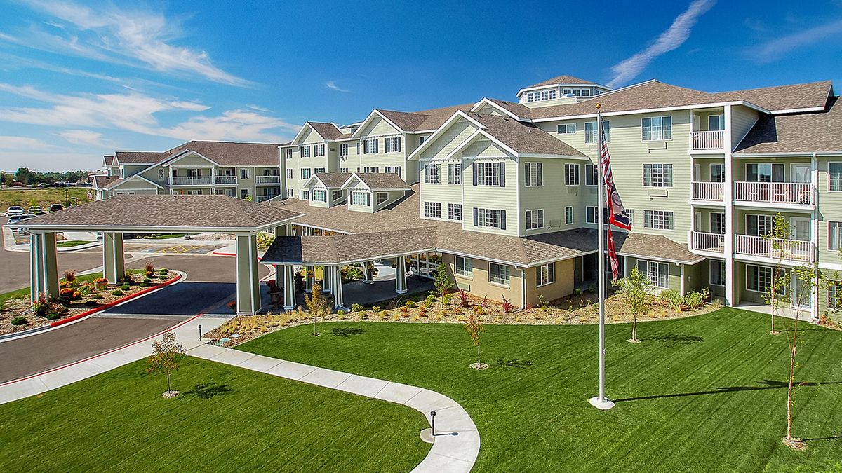 A multi-story residential building with a well-maintained lawn and flagpole under a clear blue sky.