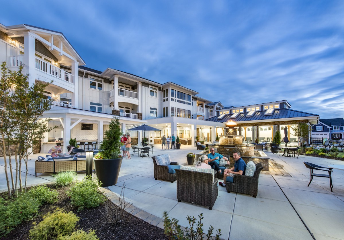 A cozy outdoor seating area in the evening, surrounded by a well-lit building and lush landscaping.