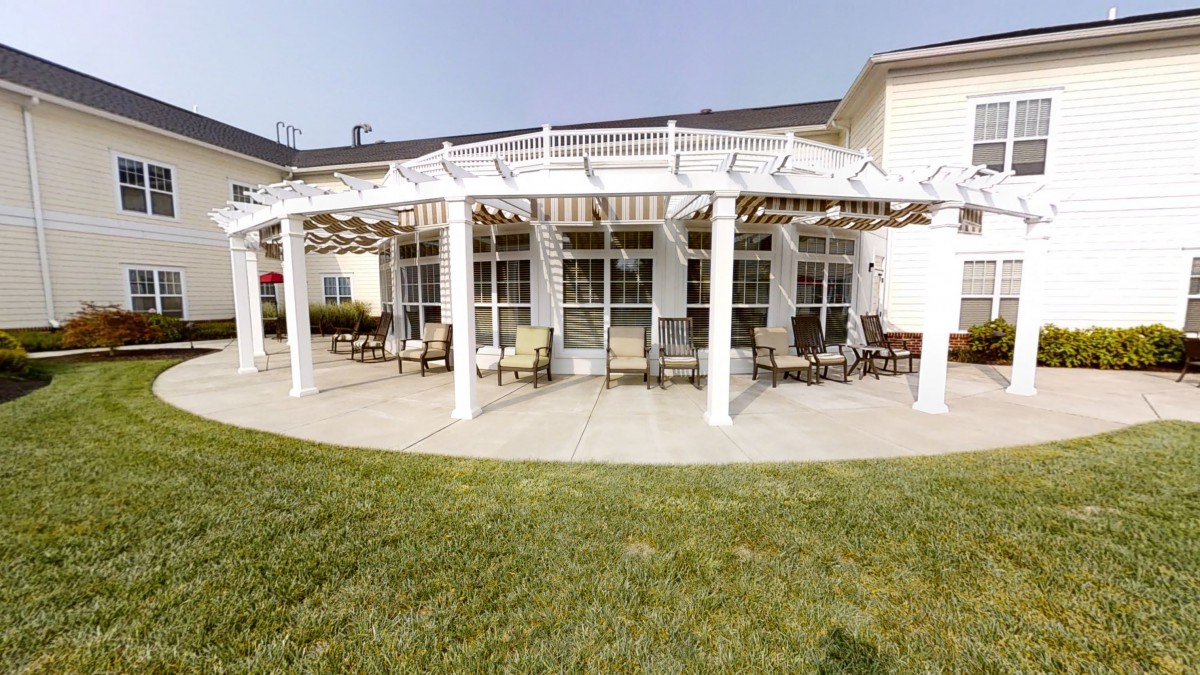 A patio area with a white pergola and outdoor seating, surrounded by a green lawn.