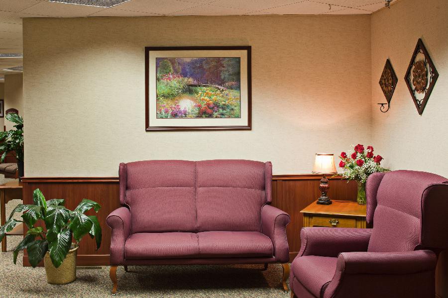 A cozy waiting room with a sofa, painting, and a table lamp.
