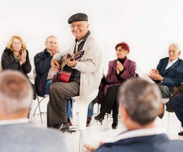 A group of elderly individuals enjoying a musical performance with guitar playing and clapping.