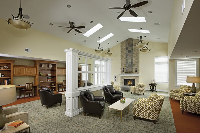 A modern living room with a cozy seating area, featuring a fireplace, ceiling fans, and skylights.