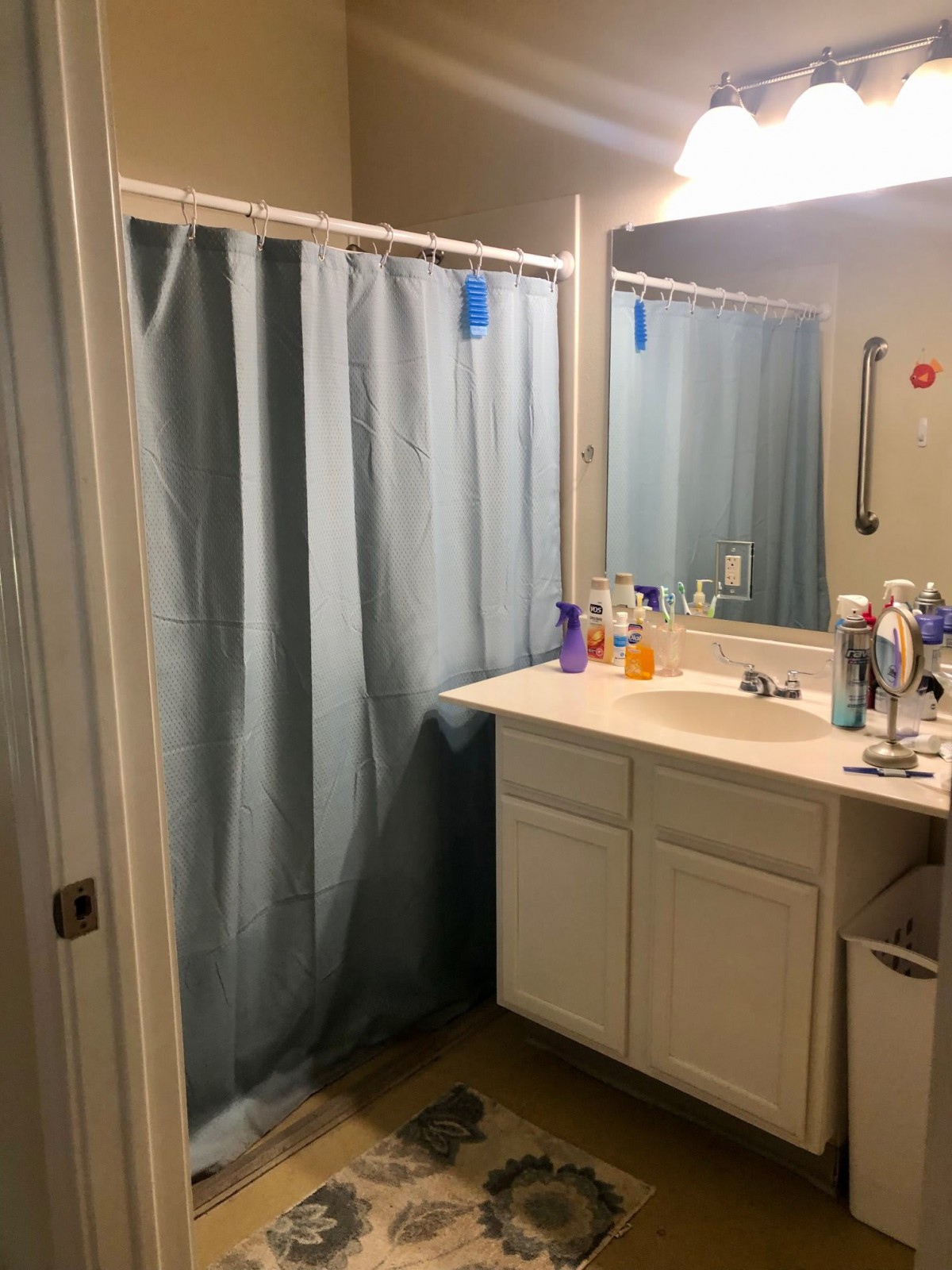 A bathroom with a shower curtain, a sink with various toiletries, and a mirror reflecting light.