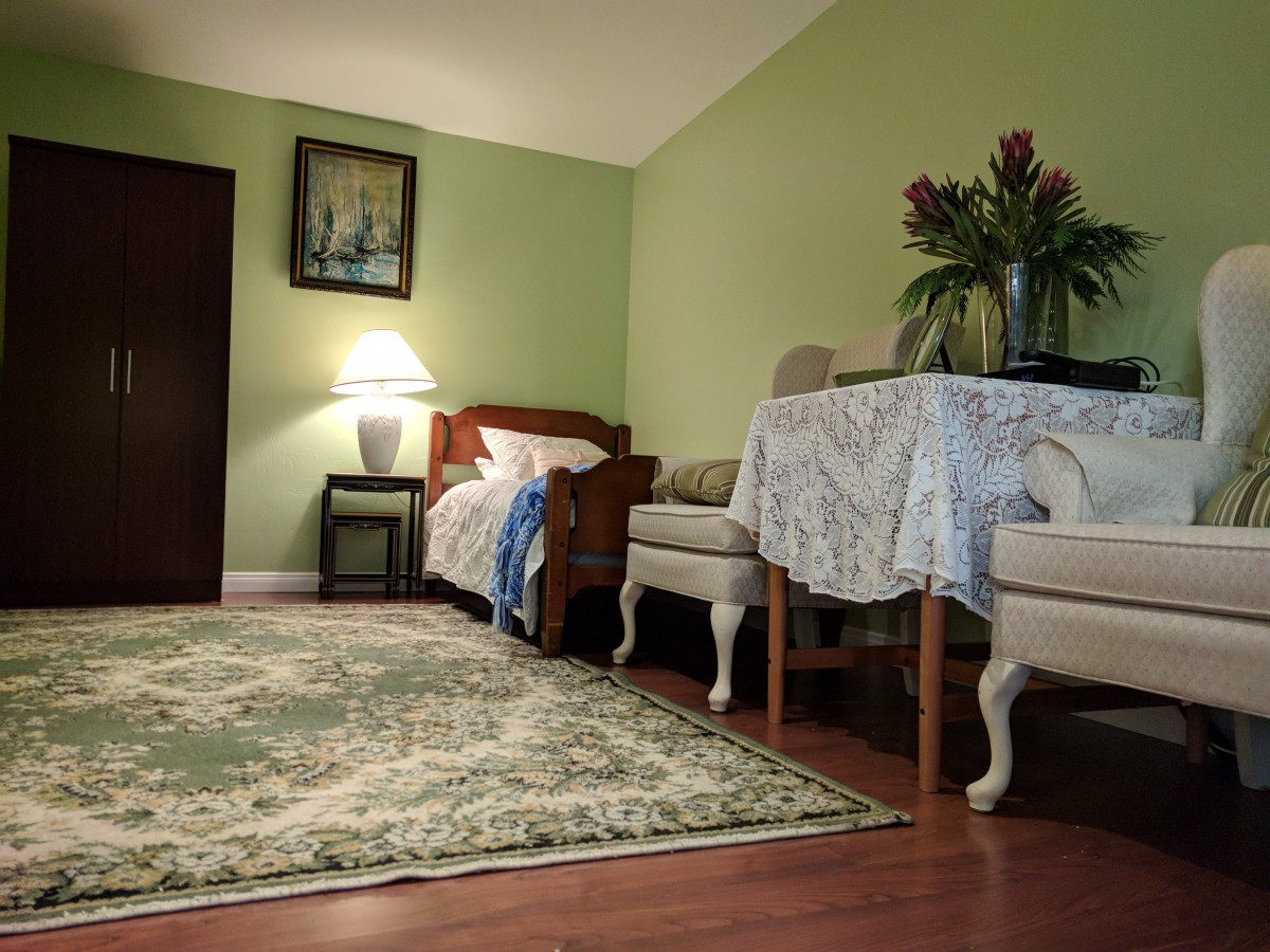A cozy living room with green walls featuring a sofa, a table with a floral arrangement, and a decorative rug.