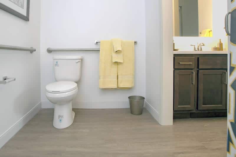 A modern minimalist bathroom with a toilet, yellow towel, sink, and mirror.