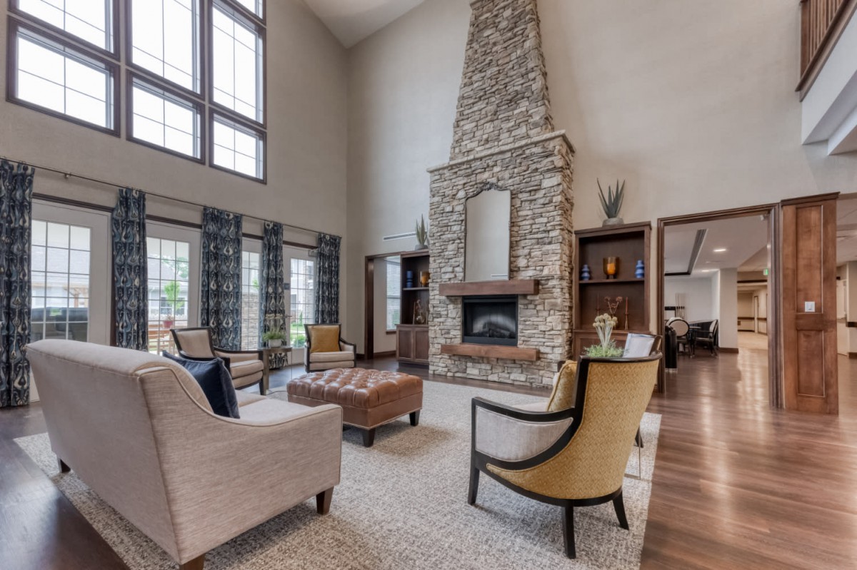 Spacious living room with a stone fireplace and high ceilings, featuring elegant furniture and large windows.