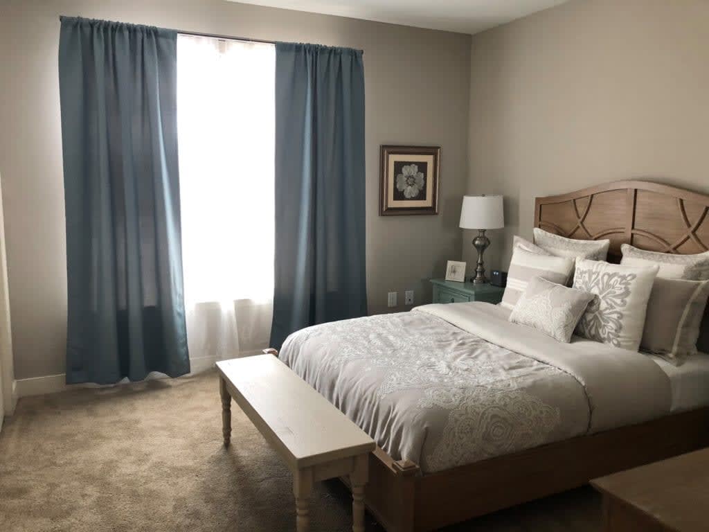 A cozy bedroom with a neatly made bed, blue curtains, and warm lighting.
