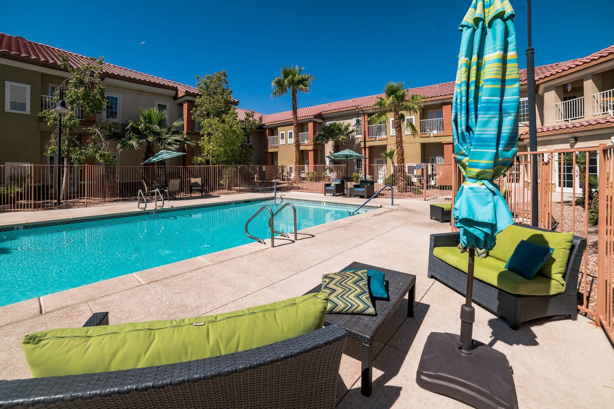 A sunny day at an apartment complex featuring a swimming pool and comfortable lounge seating.