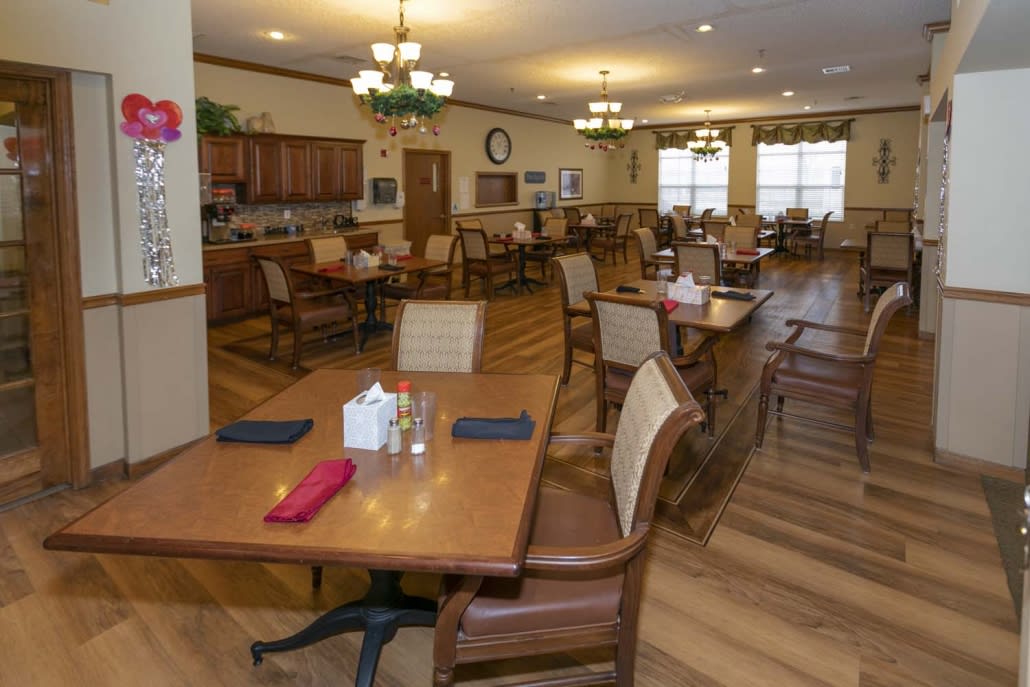 A cozy dining room with neatly arranged tables and chairs, featuring warm lighting and wood flooring.