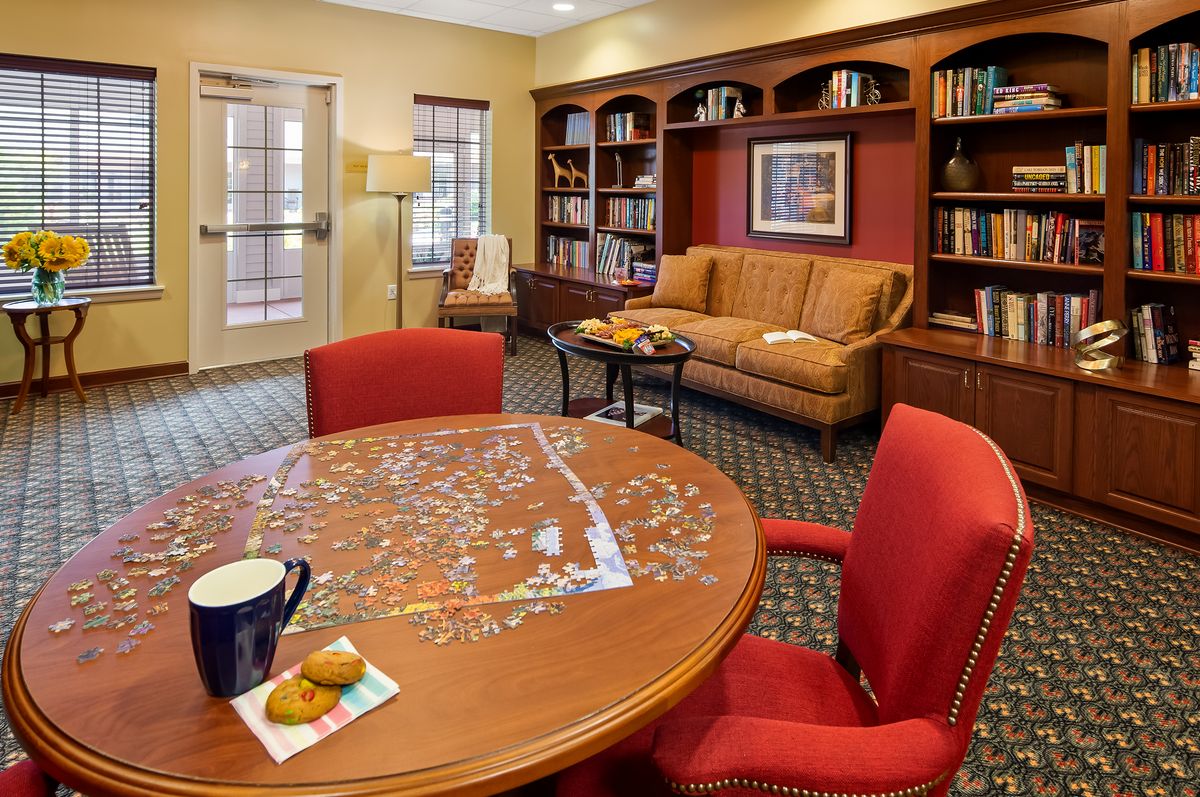 A cozy library room with bookshelves, a puzzle on the table, and comfortable seating.