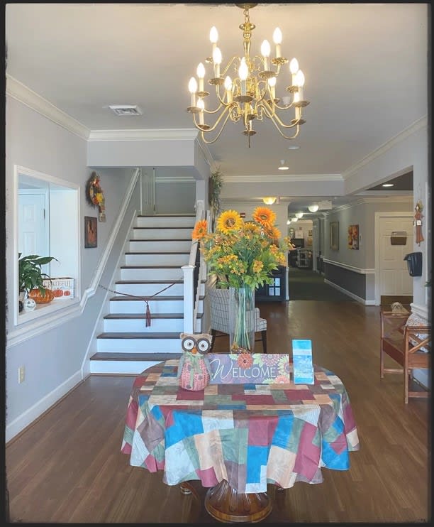 A cozy interior with a chandelier, stairs, and a table adorned with colorful sunflowers.