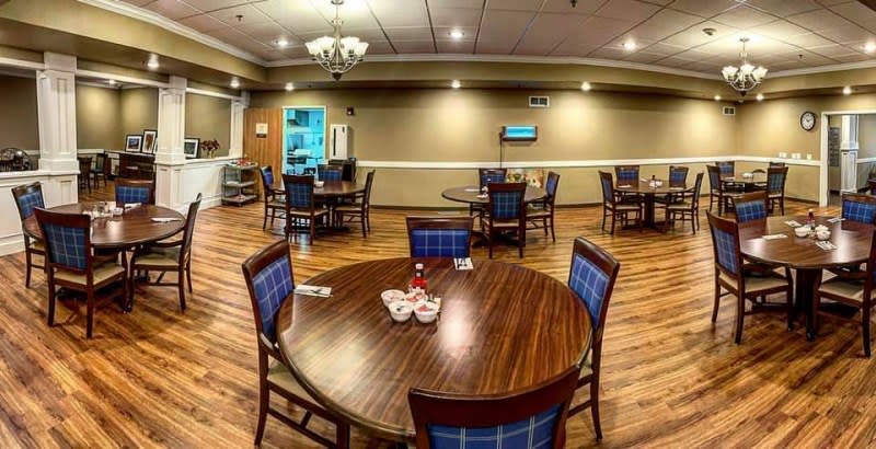 A cozy dining room with wooden tables and blue cushioned chairs, featuring warm lighting and a spacious layout.