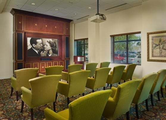 A small, intimate movie theater room with green chairs and a classic film playing on the screen.