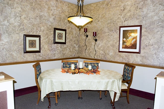 A cozy dining area with a decorative table setting, featuring wall art and a chandelier.