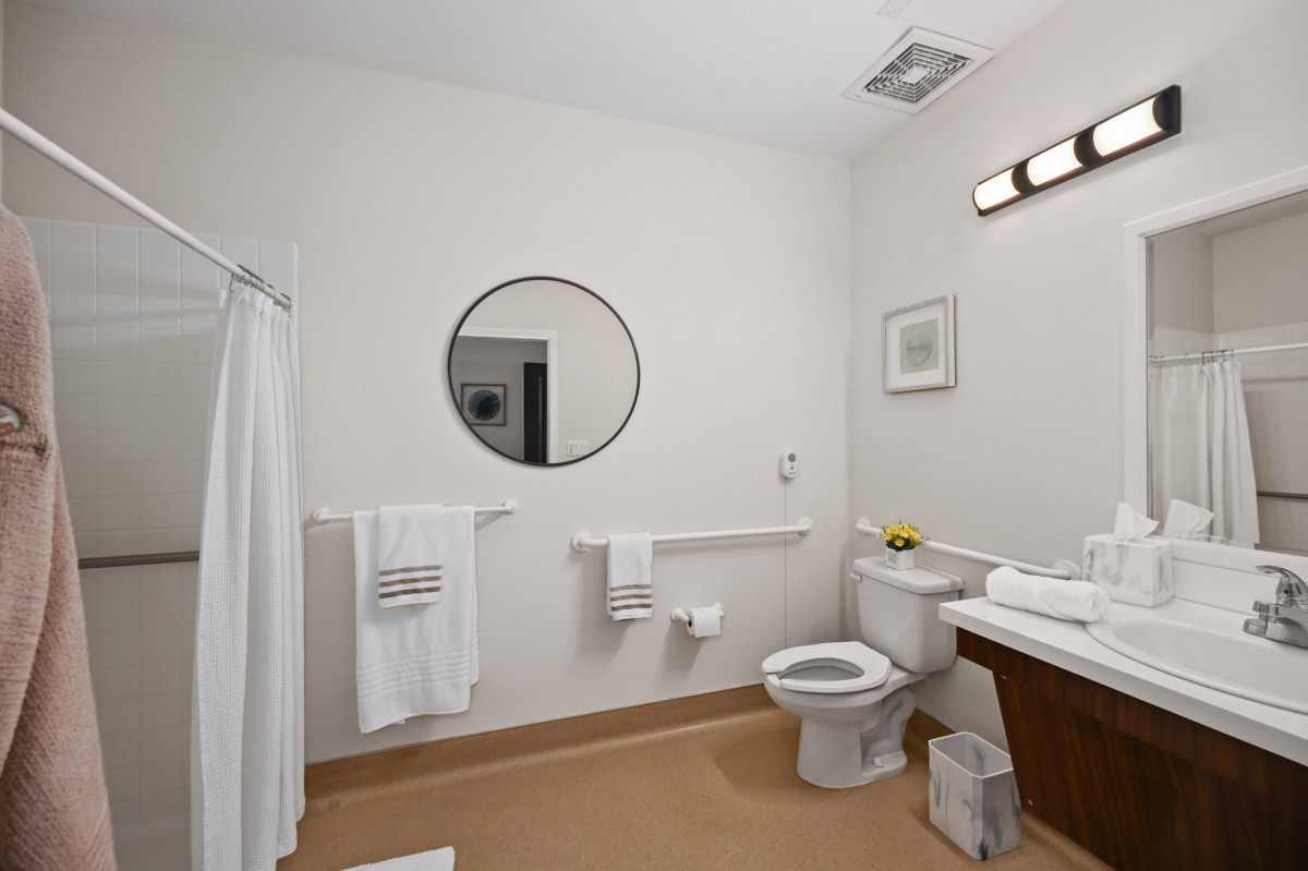 A modern and clean bathroom with a round mirror, toilet, shower, and fresh towels.