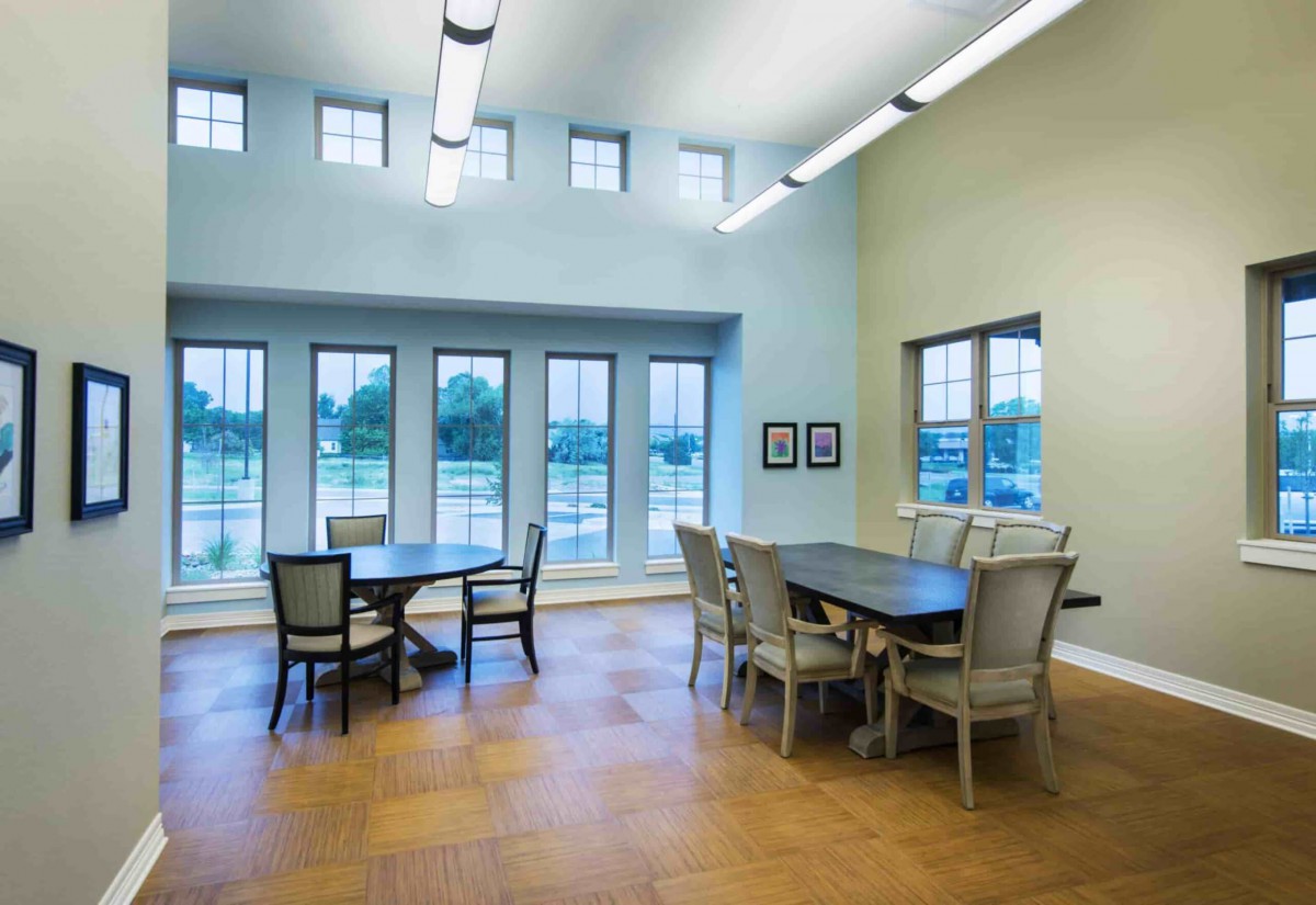 A modern dining area with tables and chairs, well-lit by natural daylight through large windows.