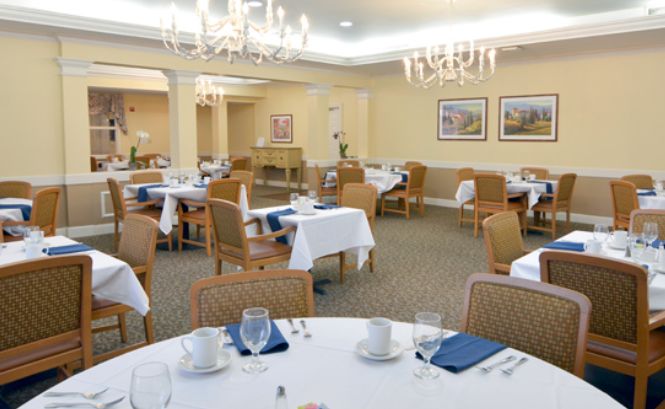 A well-appointed dining room with neatly arranged tables and chairs, illuminated by elegant chandeliers.