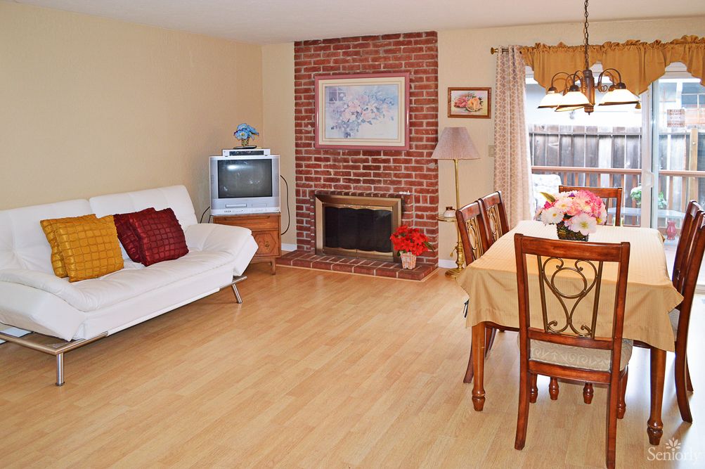A cozy living room featuring a brick fireplace, wooden flooring, a sofa, and a dining table.