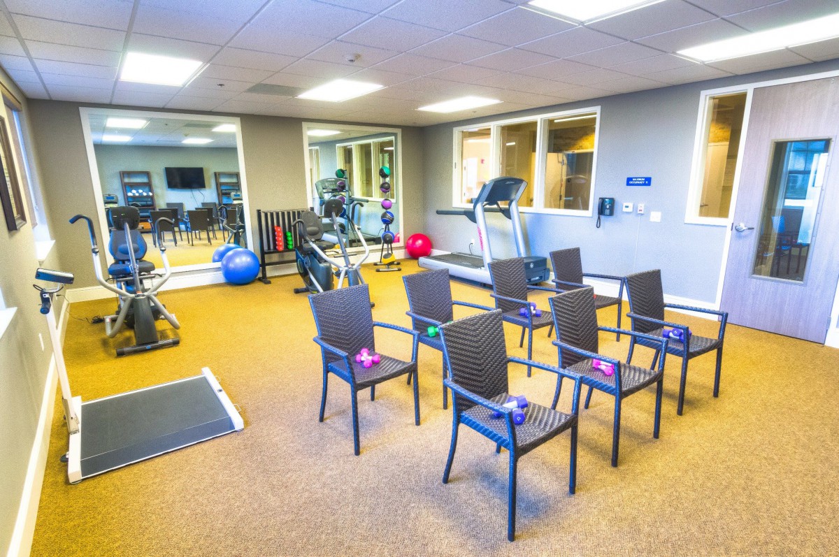 A well-equipped gym with exercise machines and chairs arranged in rows.